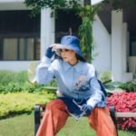 Stylish woman in vibrant outfit posing on a bench in a sunny Bandung park.