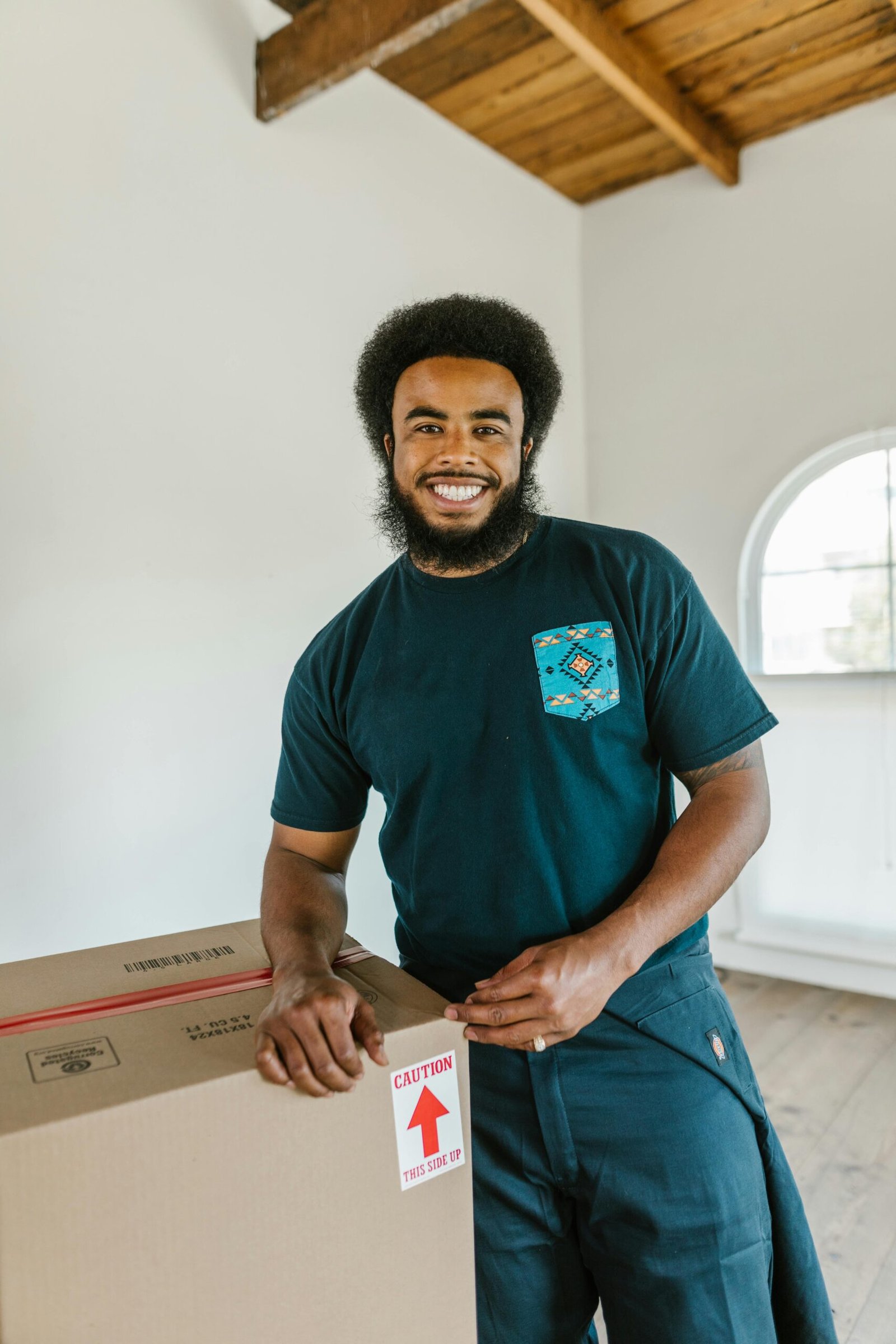 Friendly man with afro hair and beard standing in a bright room holding a moving box.