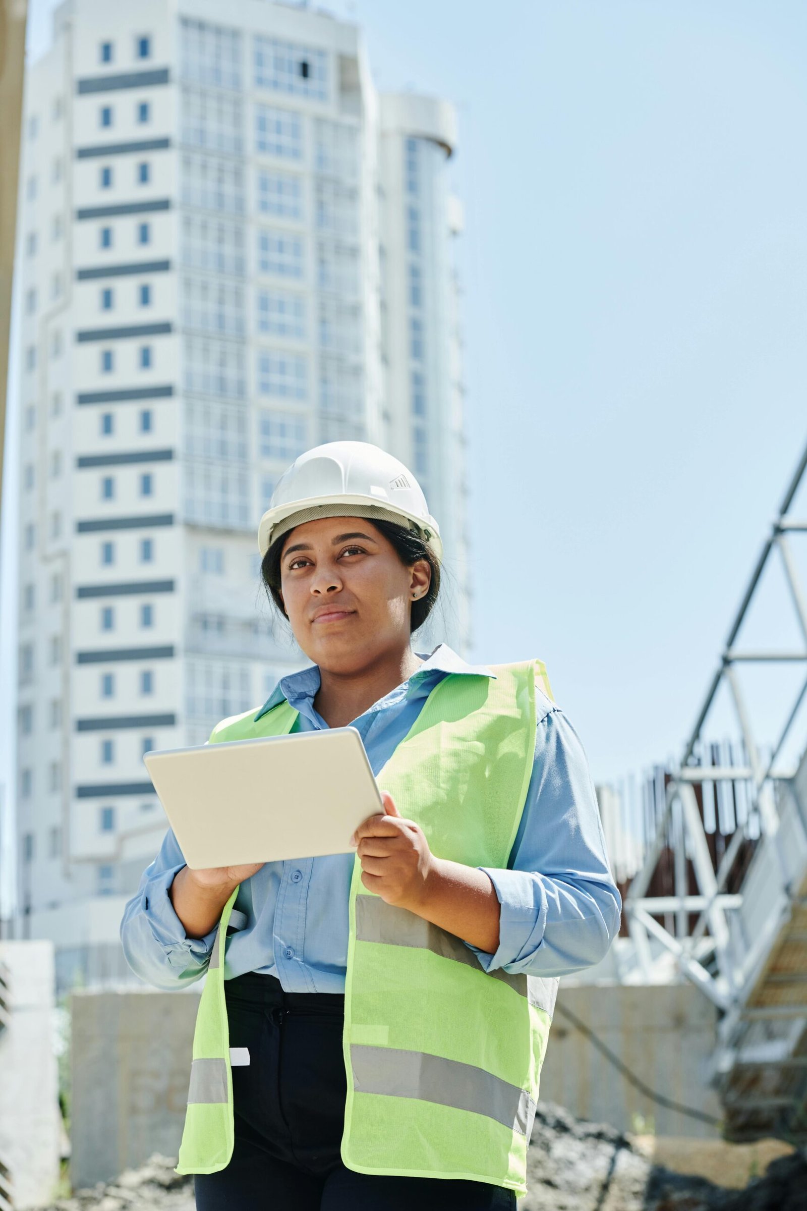 Woman in protective gear managing construction site with tablet in city.